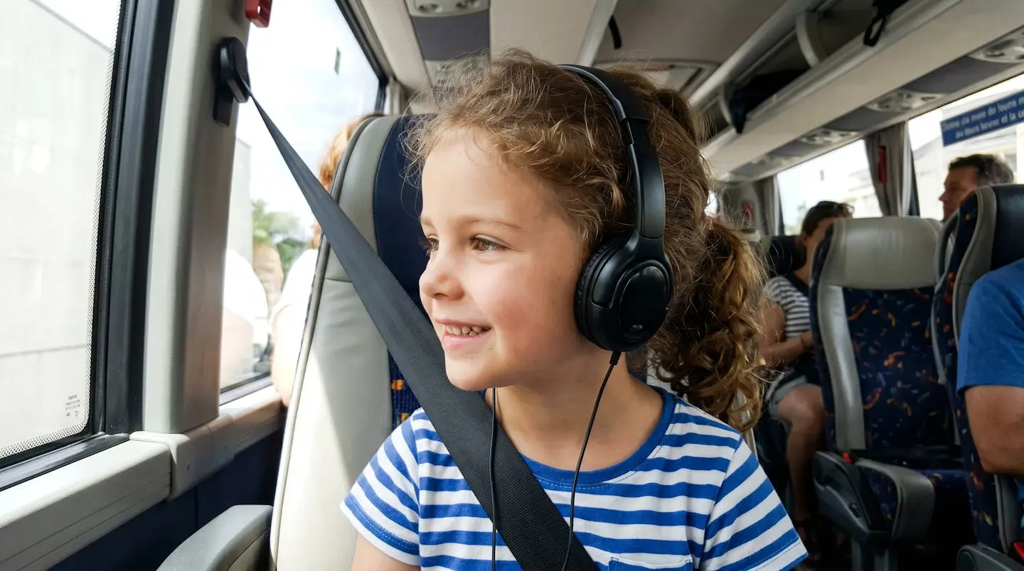 Un enfant de profil portant un casque audio noir écoute attentivement les commentaires à bord d'un bus touristique moderne, avec une expression concentrée et souriante